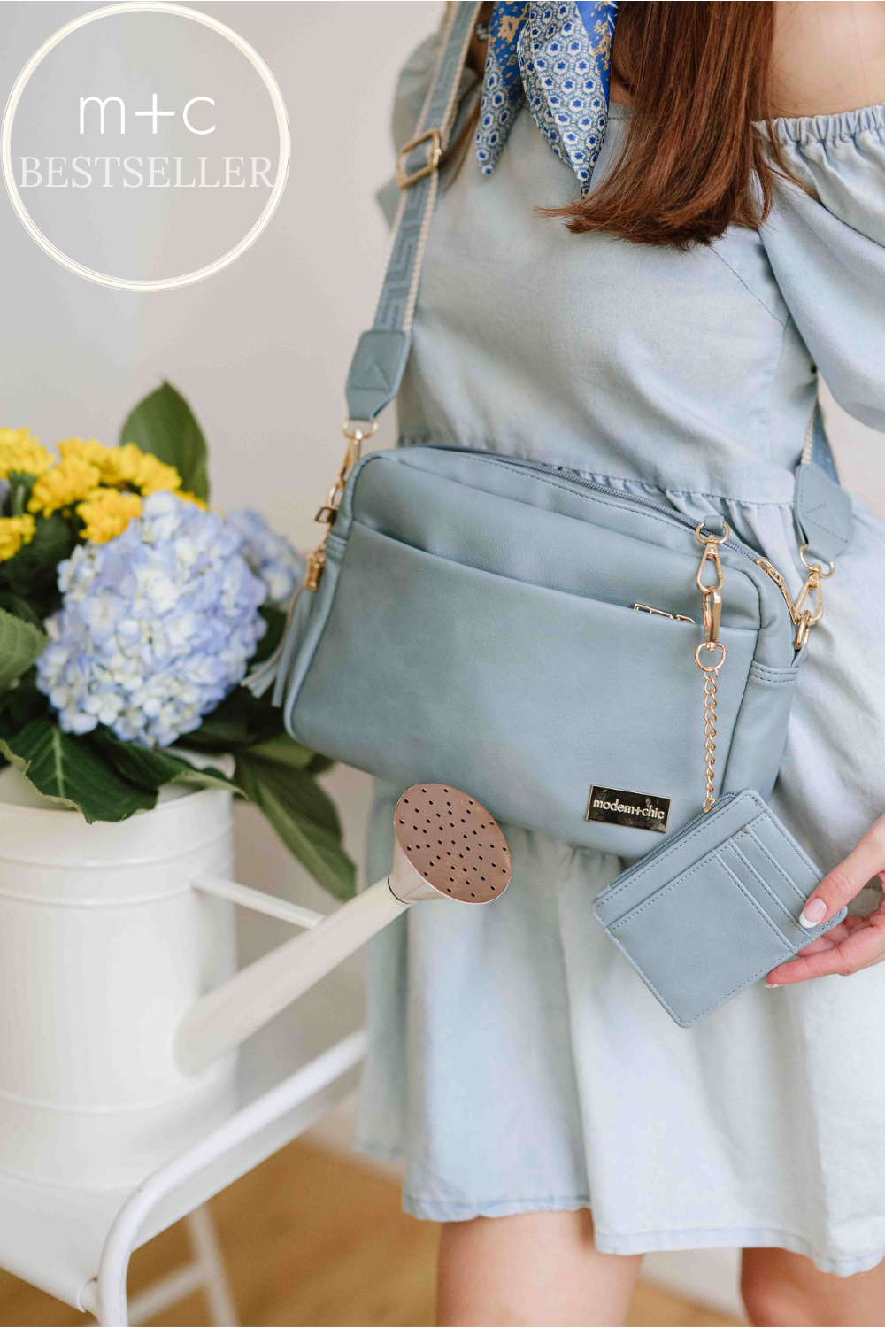 Woman wearing a blue dress wearing a dusty blue Modern + Chic Alice Crossbody Vegan Leather bag.