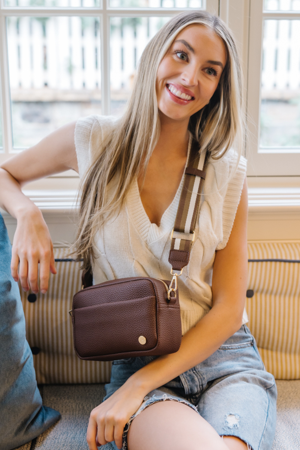 Woman wearing a brown Modern+Chic Willow Vegan Leather Convertible Crossbody Bag on a white background. 