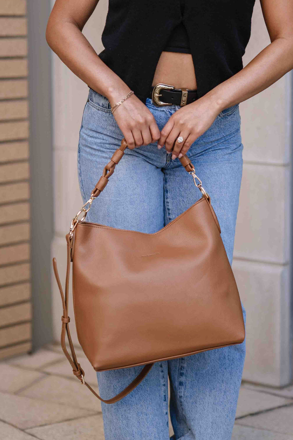 Woman holding a camel Modern+Chic Sawyer Convertible Slouchy Tote Bag for Women with a vegan leather braided shoulder strap as an adjustable crossbody strap hangs. 