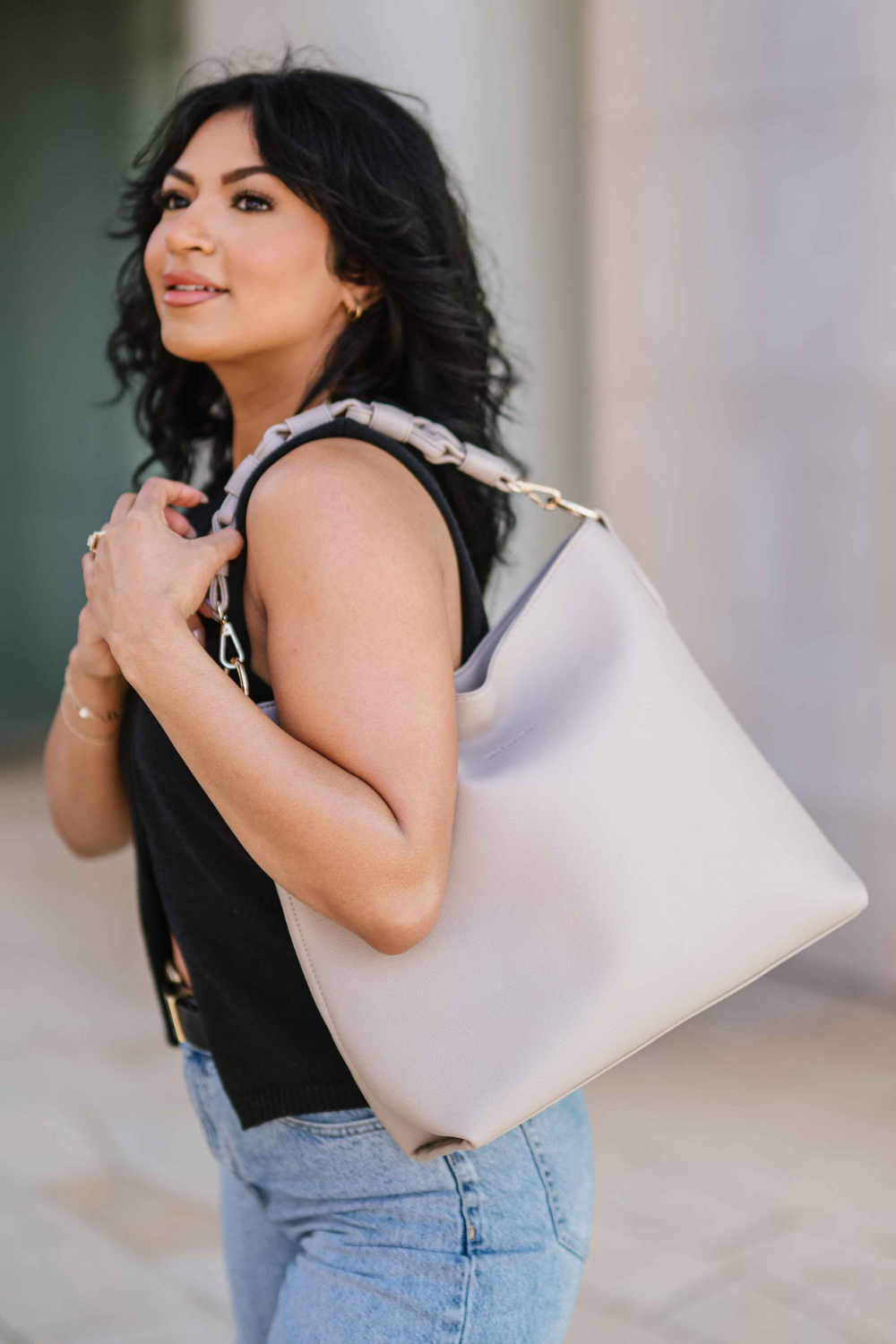 Woman wearing a beige Modern+Chic Sawyer Convertible Slouchy Tote Bag for Women with a vegan leather braided shoulder strap against a neutral background. 