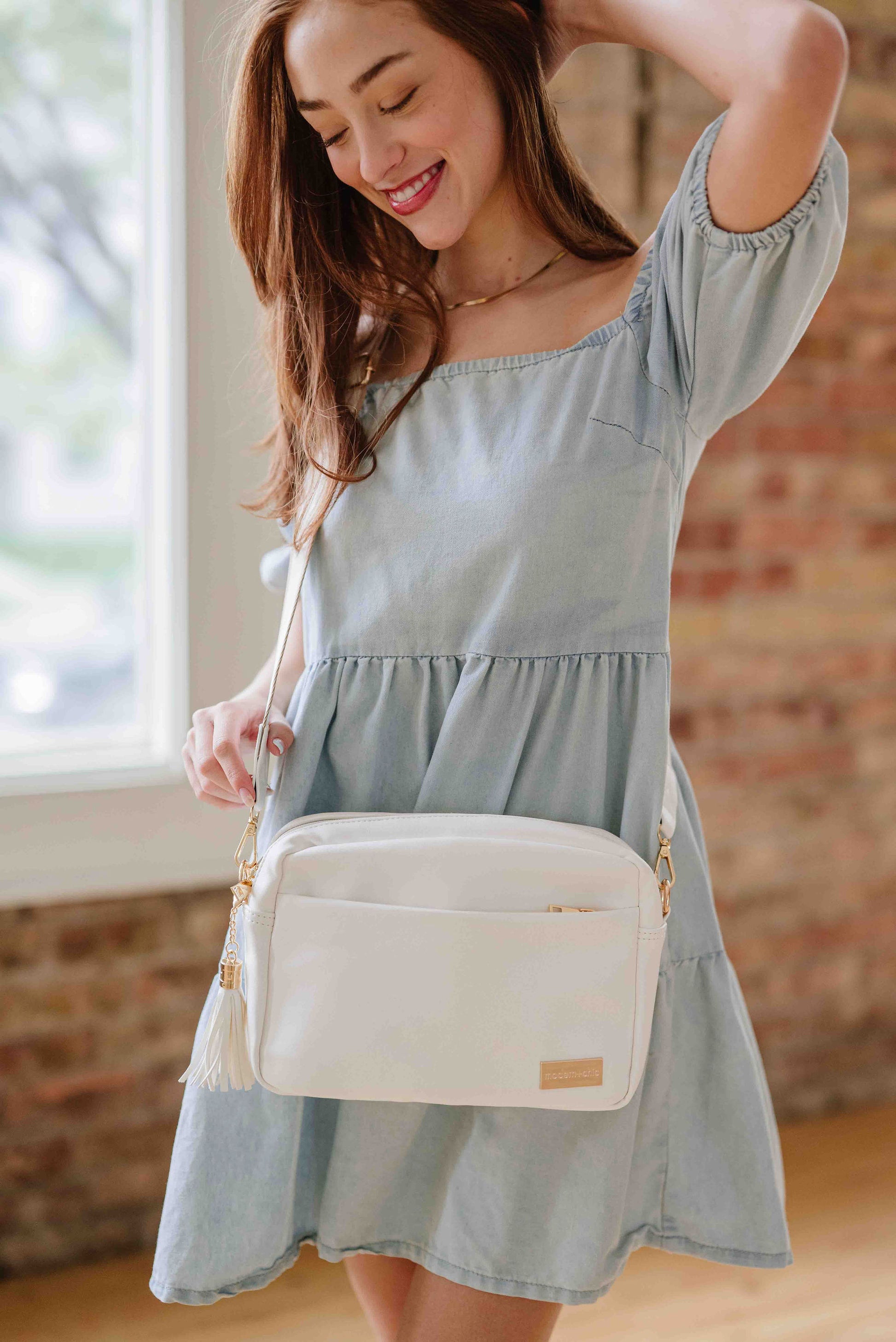 Red-haired woman wearing a white Modern + Chic Alice Crossbody vegan leather bad with gold hardware over her shoulder. 