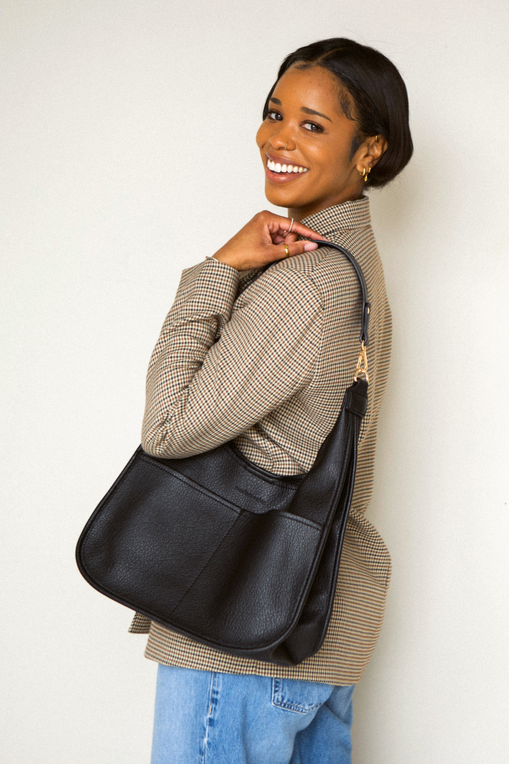 Woman holding a black  Modern+Chic Clara Vegan Leather Slouchy Tote Bag for Women on a white background. 