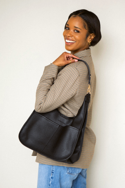 Woman holding a black  Modern+Chic Clara Vegan Leather Slouchy Tote Bag for Women on a white background. 
