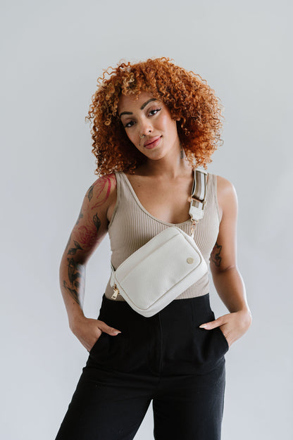 Woman wearing a cream Modern+Chic Willow Vegan Leather Convertible Crossbody Bag on a white background. 
