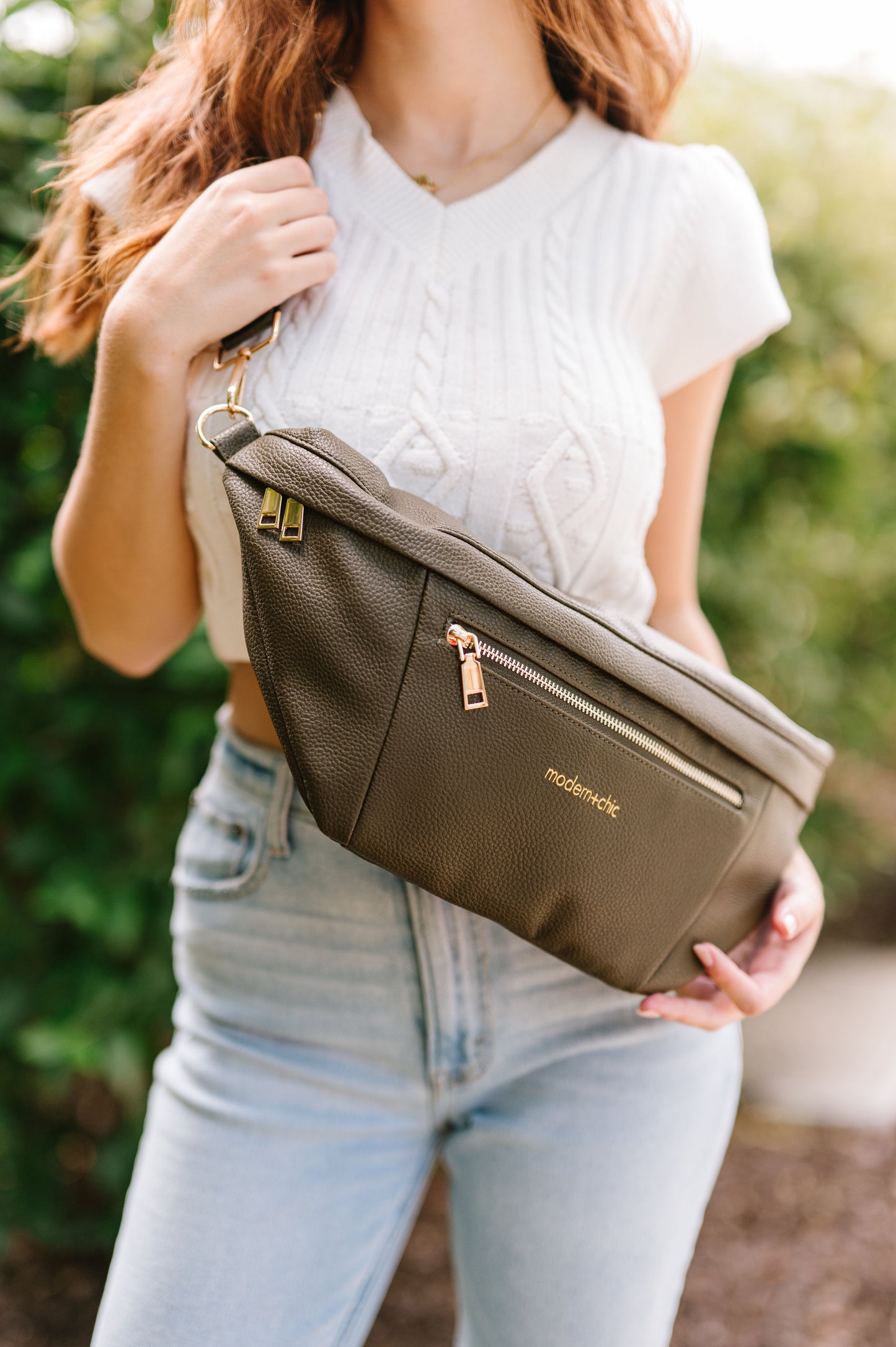 A woman wearing a cropped white sweater vest and an oversized olive Modern+Chic Presley Oversized Sling Bag for Women with gold hardware across her torso.