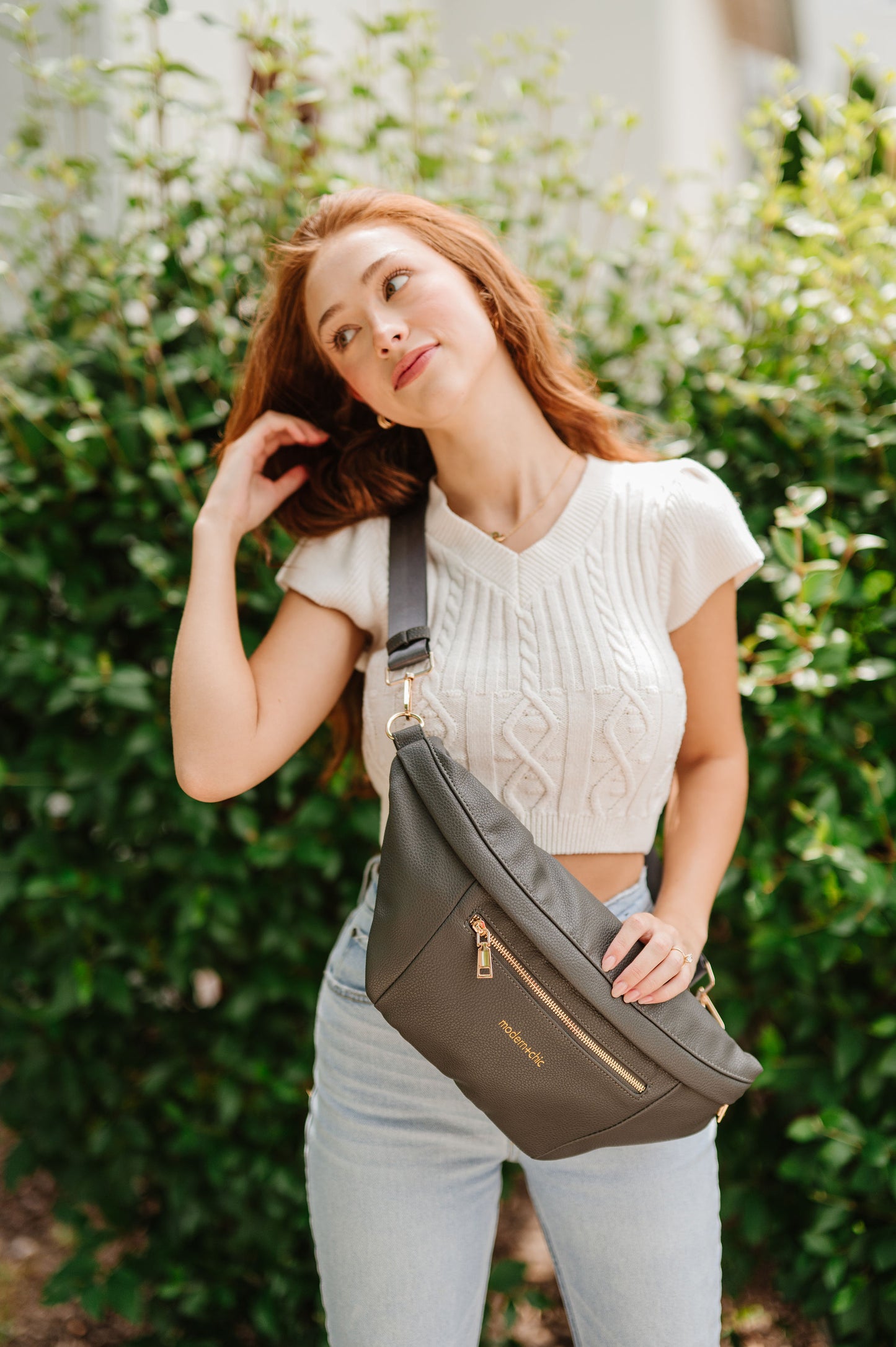 A woman wearing a cropped white sweater vest and an oversized olive Modern+Chic Presley Oversized Sling Bag for Women with gold hardware across her torso.