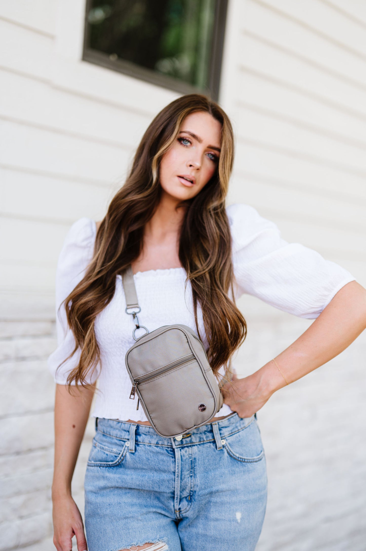 Woman wearing a white top, jeans and a grey Modern + Chic Lainey Convertible Crossbody Bag for Women crossbody.