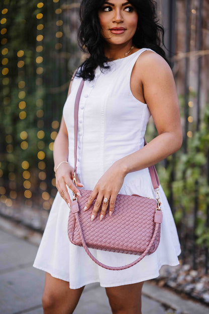 Woman in a white dress holding a pink Modern + Chic Elle Woven Crossbody Bag for Women outdoors.