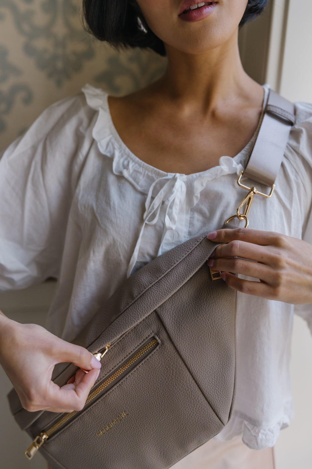 A woman wearing an oversized taupe Modern+Chic Presley Oversized Sling Bag for Women with gold hardware across her torso.