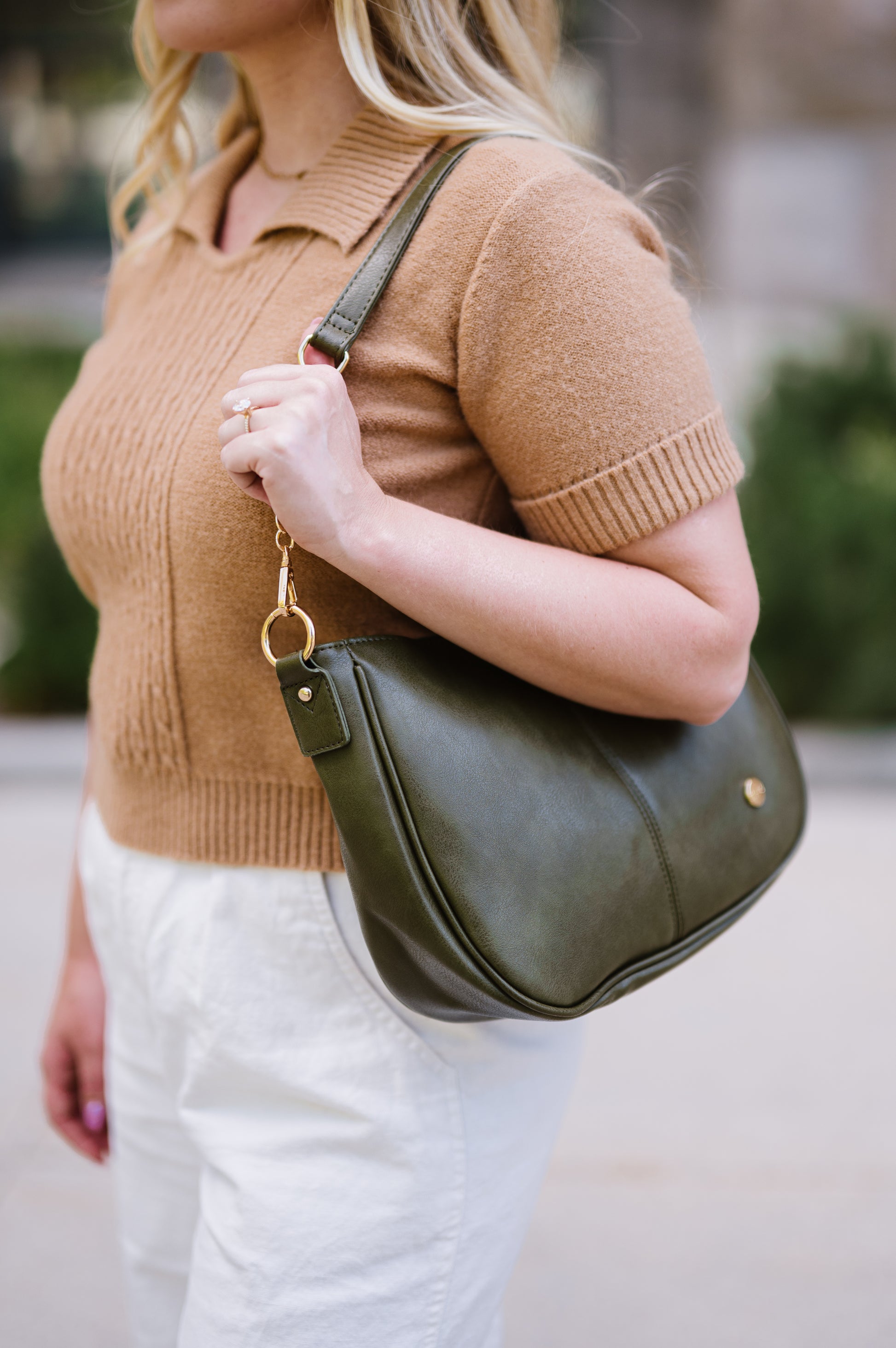 Woman holding an olive green Marissa Modern + Chic vegan leather crossbody handbag worn with a shorter strap as an over the shoulder handbag. 