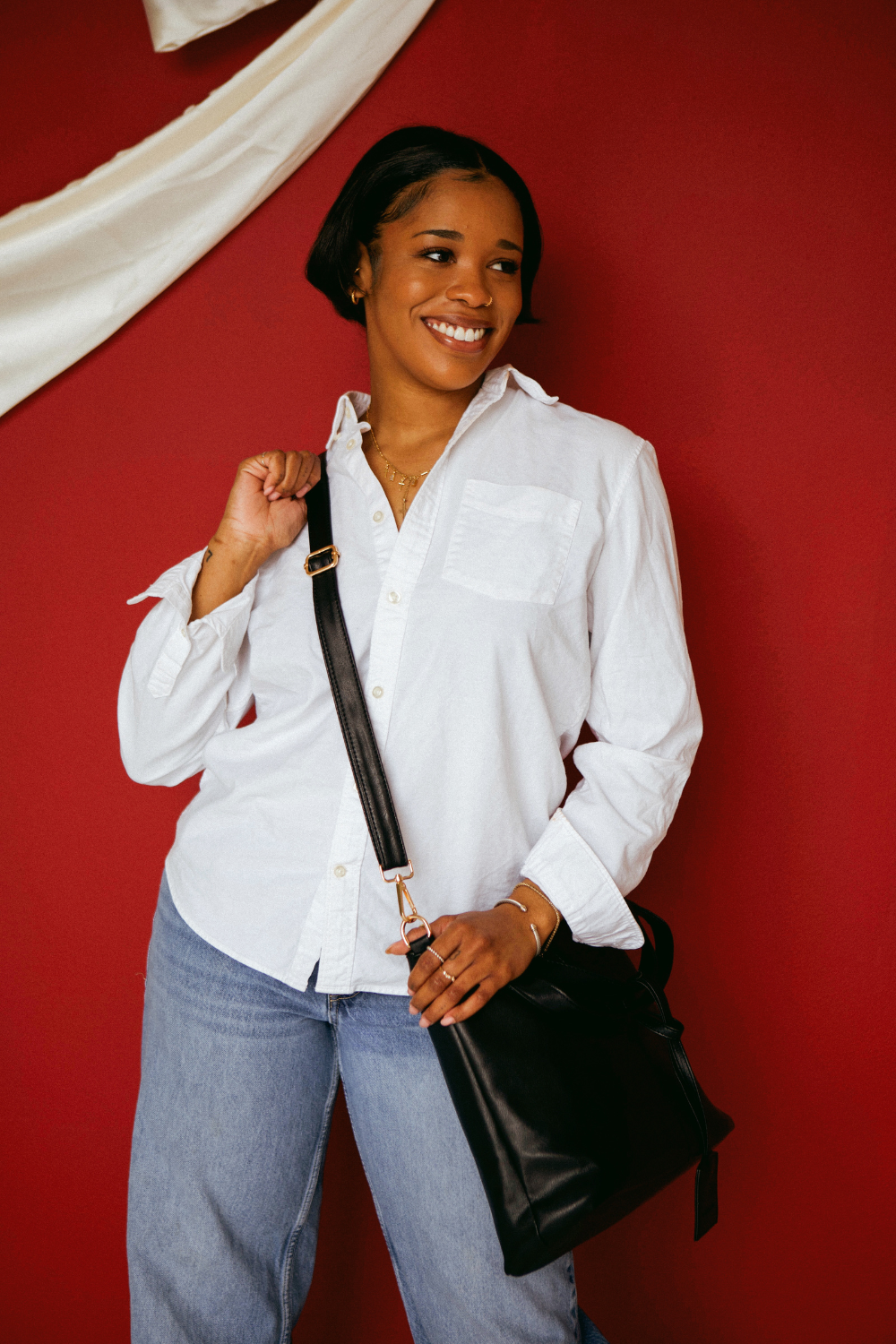 A woman wearing a white button up shirt with jeans and a black Modern+Chic Olivia Convertible Slouchy Tote Bag for Women across her body. 