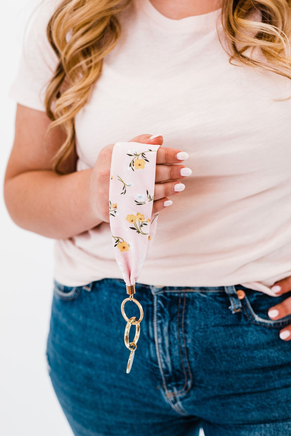 A woman wearing a white tee shirt and jeans holding a white floral printed Modern + Chic Luna Fabric Keychain Bracelet for Women.