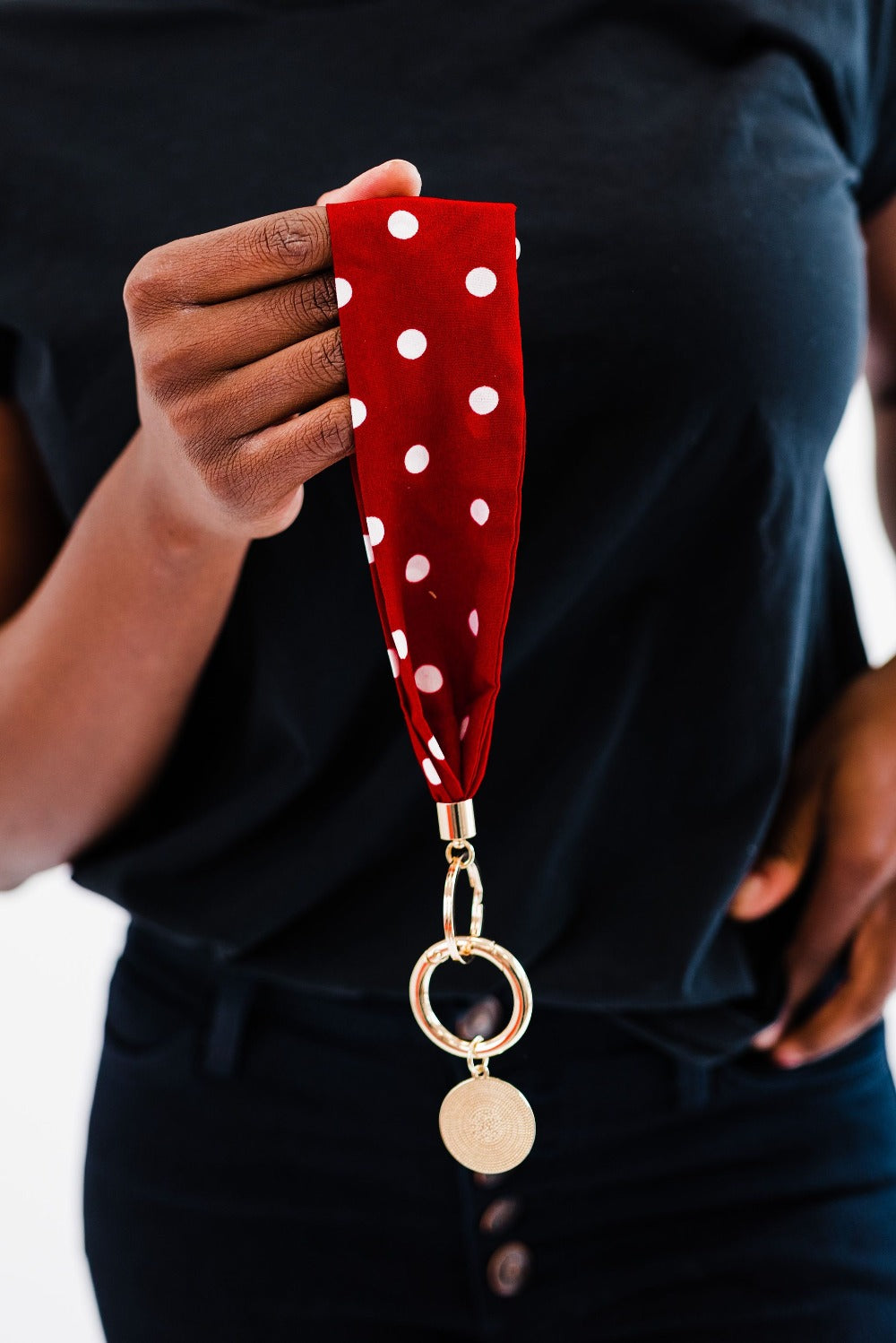A woman wearing all black holding a red and white polka dot Modern + Chic Luna Fabric Keychain Bracelet for Women her hand.
