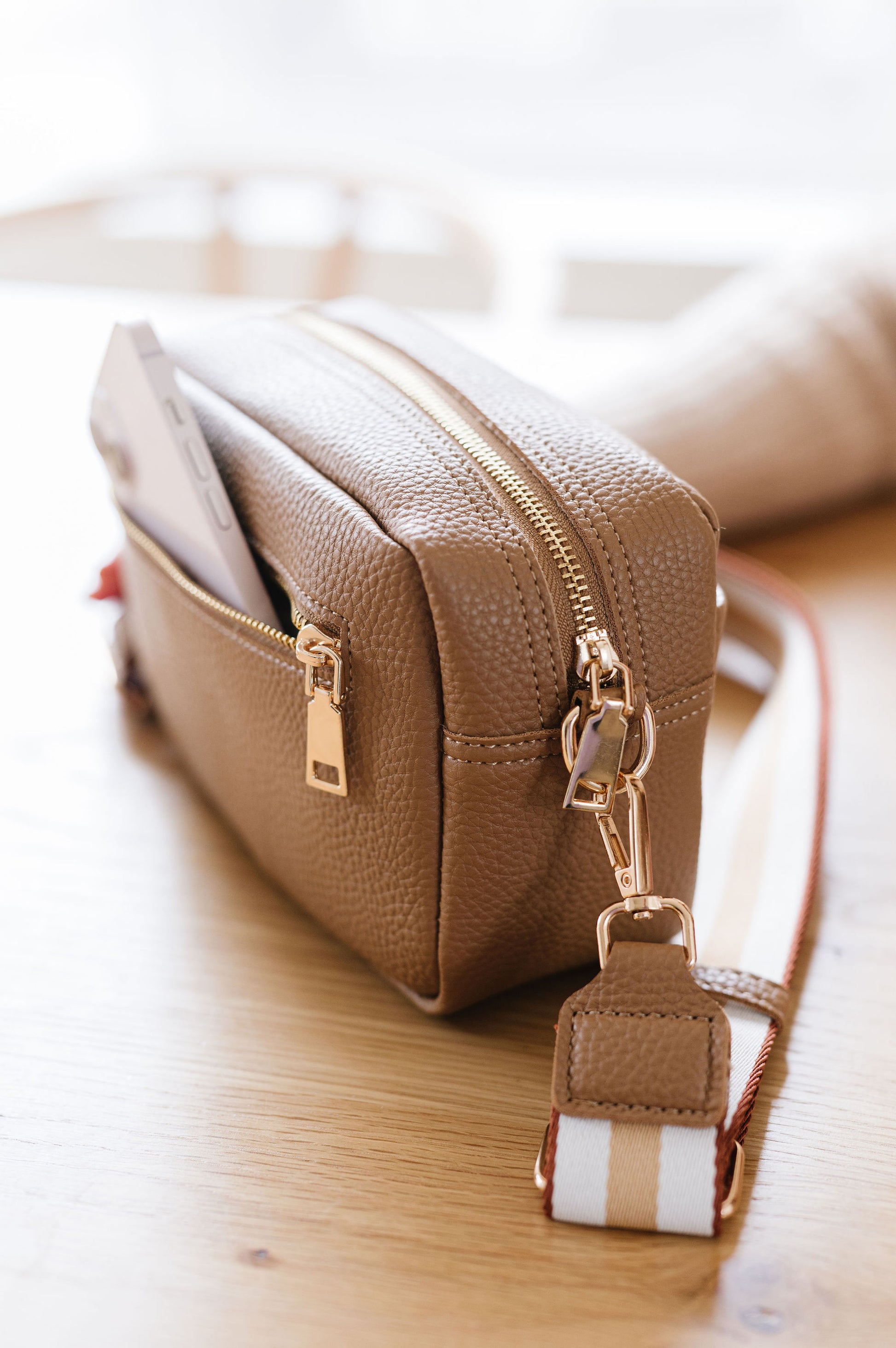 A beige Modern+Chic Willow Vegan Leather Convertible Crossbody Bag on a desk.