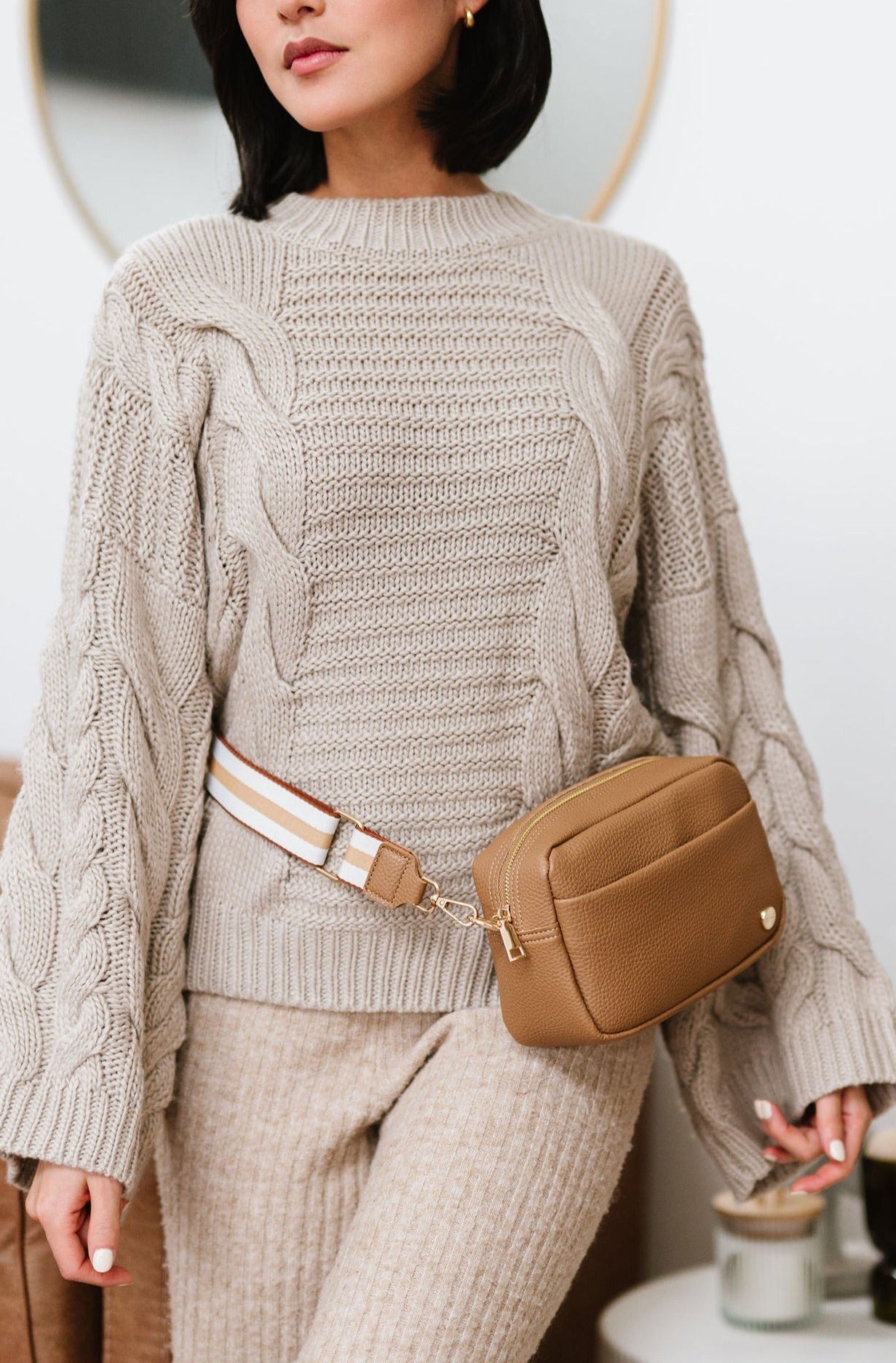 Woman wearing a beige Modern+Chic Willow Vegan Leather Convertible Crossbody Bag around her waist as a belt bag. 