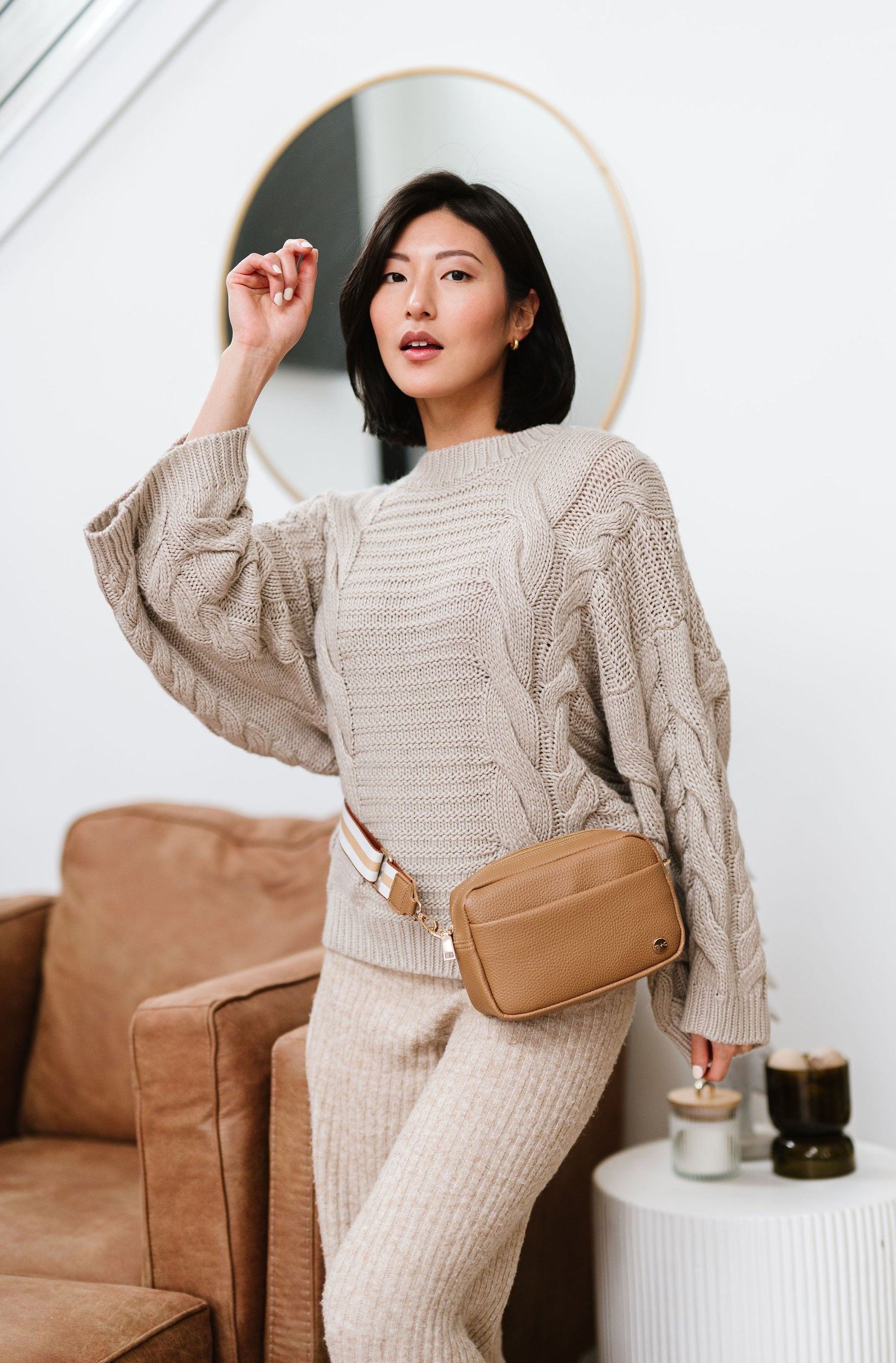 Woman wearing a beige Modern+Chic Willow Vegan Leather Convertible Crossbody Bag around her waist like belt bag. 